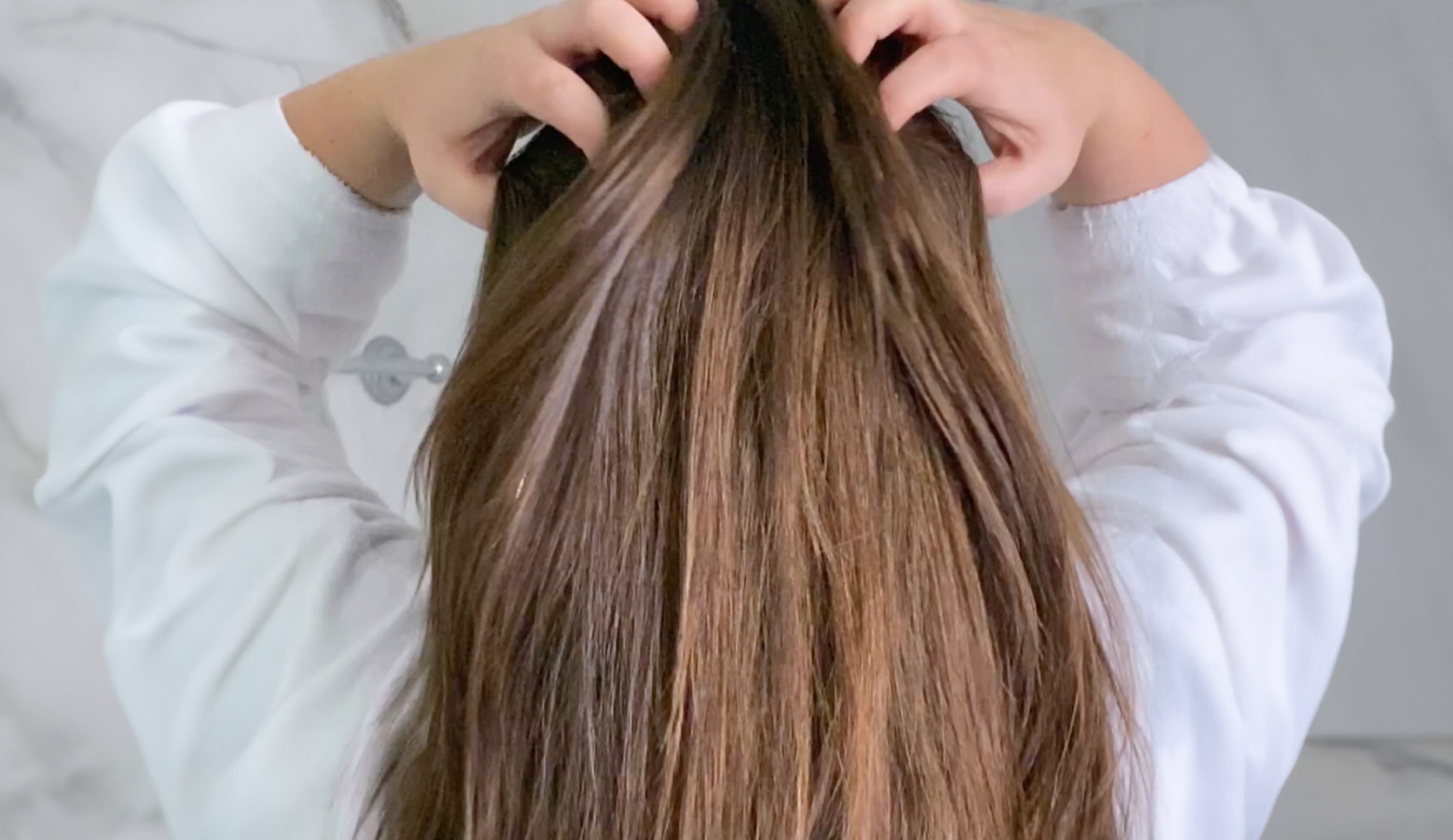 Brunette woman runs her hands through her long, shiny and healthy looking hair.