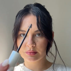 Woman holding Nulastin Brow serum applicator in front off her face