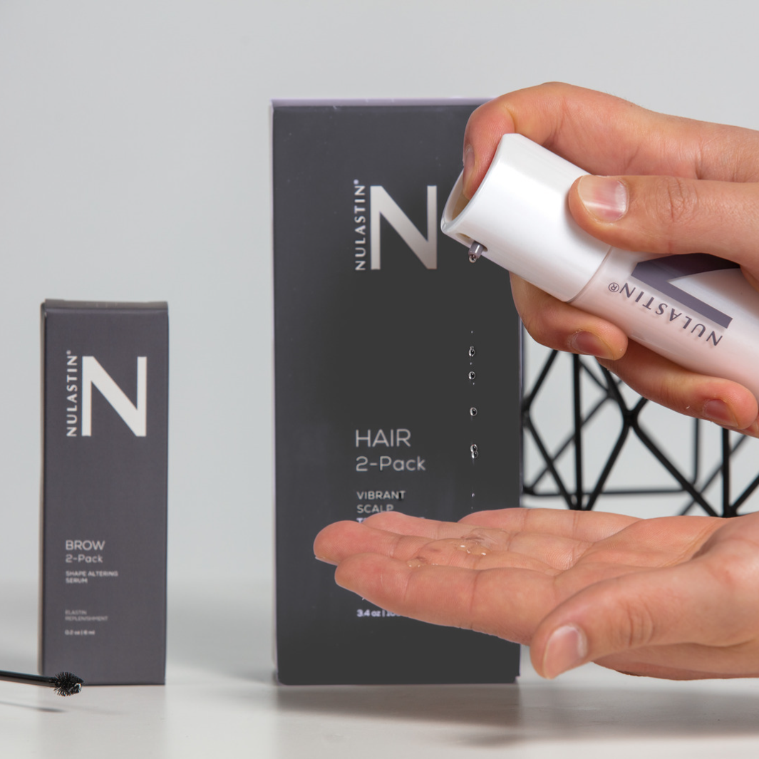 Hands applying NULASTIN hair treatment to hands in front of grey packaging 