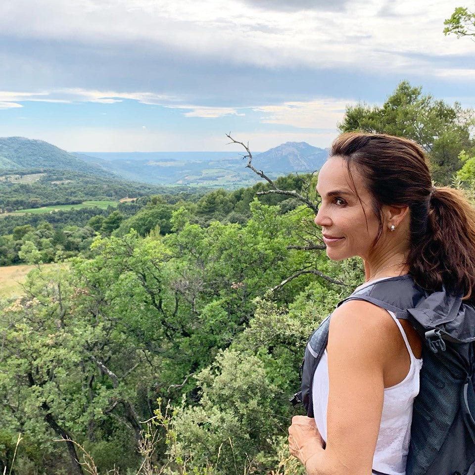 Woman hiking on a ridge looking over a green valley and distant mountains, wearing a backpack