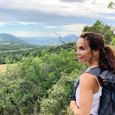 Woman hiking on a ridge looking over a green valley and distant mountains, wearing a backpack