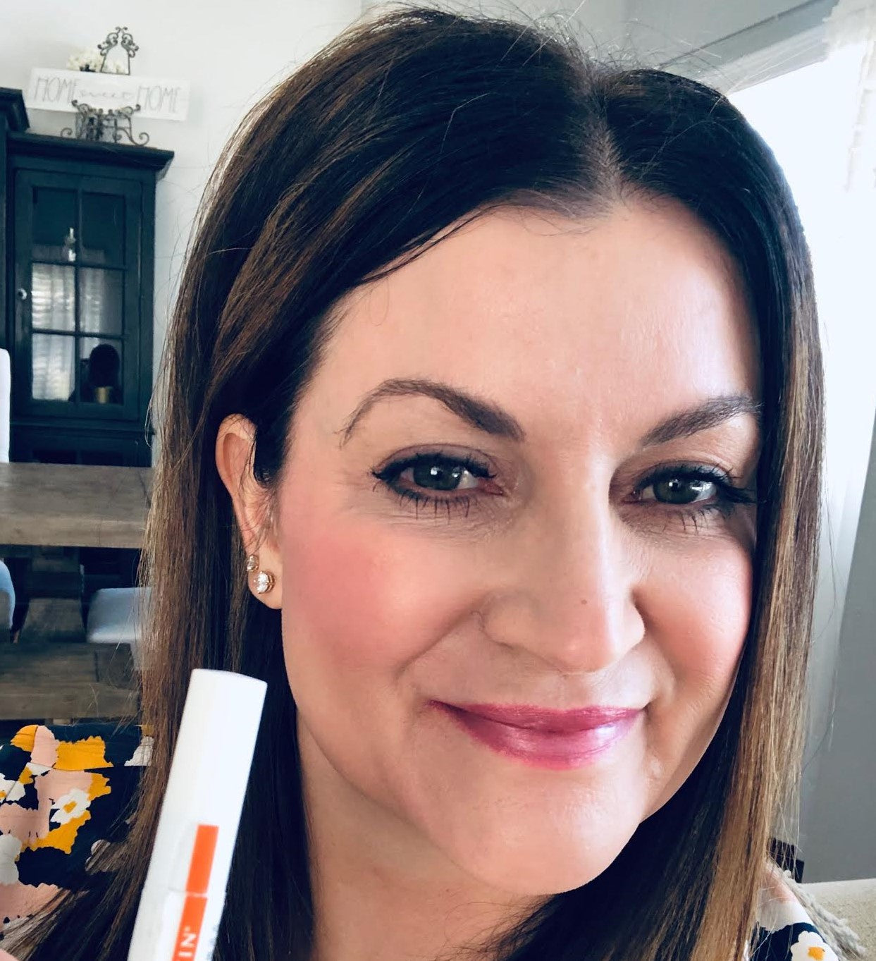 Smiling woman holding a NULASTIN serum tube near her face in a home setting