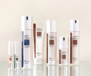Front view of assorted NULASTIN hair and skin serums and cleansers on a reflective surface