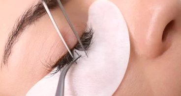 Close-up of a technician applying individual eyelash extensions with tweezers and an under-eye gel pad