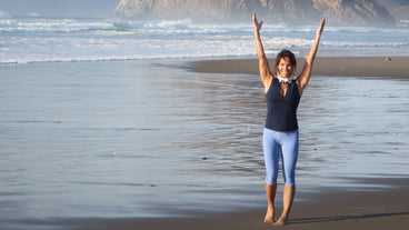 Woman raising her arms and smiling on a wet sandy beach with ocean waves and a rocky headland in the background