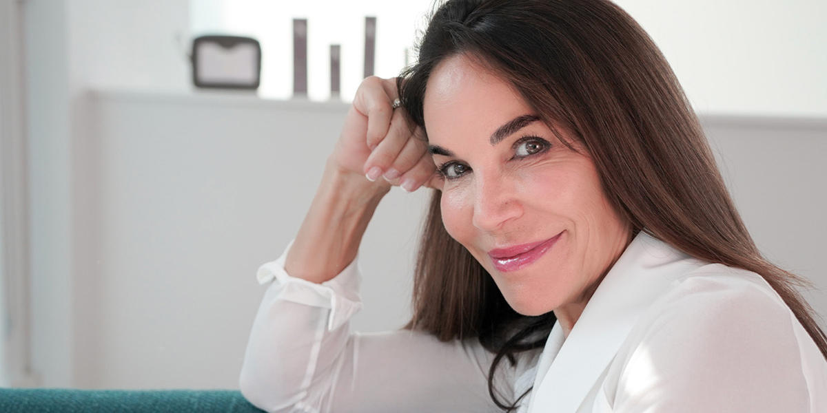 Smiling woman with long brown hair leaning on her hand in a bright, relaxed indoor setting