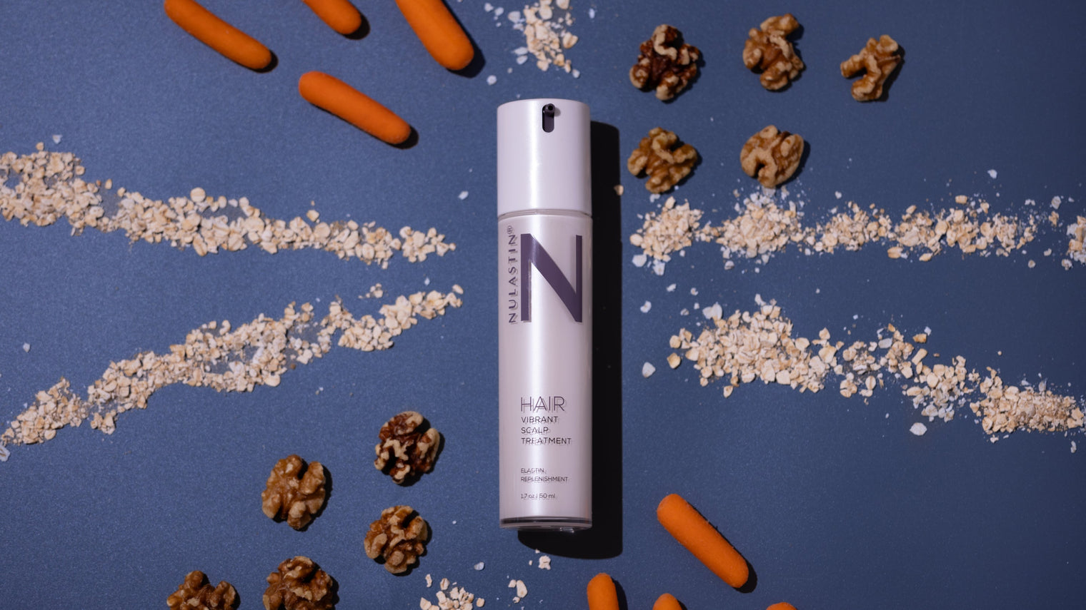 Top-down view of NULASTIN Hair Scalp Treatment bottle among oats, walnuts, and baby carrots on dark blue background