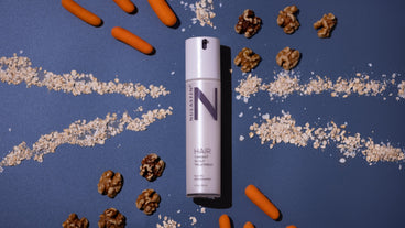 Top-down view of NULASTIN Hair Scalp Treatment bottle among oats, walnuts, and baby carrots on dark blue background