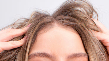 Close-up of a person parting light brown hair to reveal the hairline and scalp