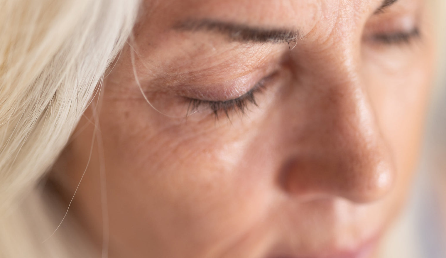 Close-up of a woman's face with eyes closed, relaxed expression and light blond hair in soft natural lighting
