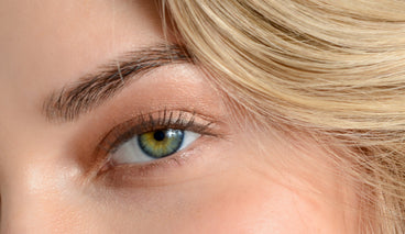 Close-up of a green-hazel eye and natural eyebrow showing fuller brow hairs and soft neutral eyeshadow with blonde hair framing the face