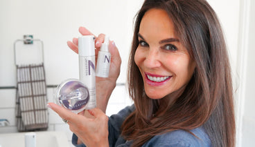 Founder smiling while holding NULASTIN hair treatment bottles and a scalp scrubber in a bright bathroom