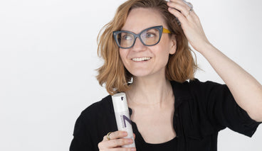Woman smiling while holding a NULASTIN serum bottle near her chest against a plain white background