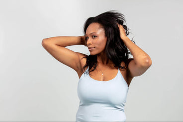 Woman running her hands through long dark hair, wearing a light blue fitted tank top against a light gray background