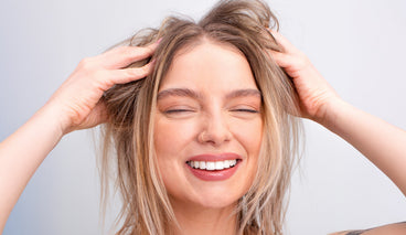 Young woman lifting her hair with both hands in a close-up, smiling to show her blonde hair and scalp