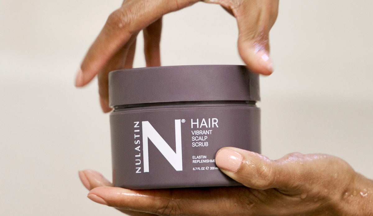Close-up front view of Vibrant Scalp Scrub jar 6.7 fl oz showcasing label and screw-top lid held in wet hands against a neutral background