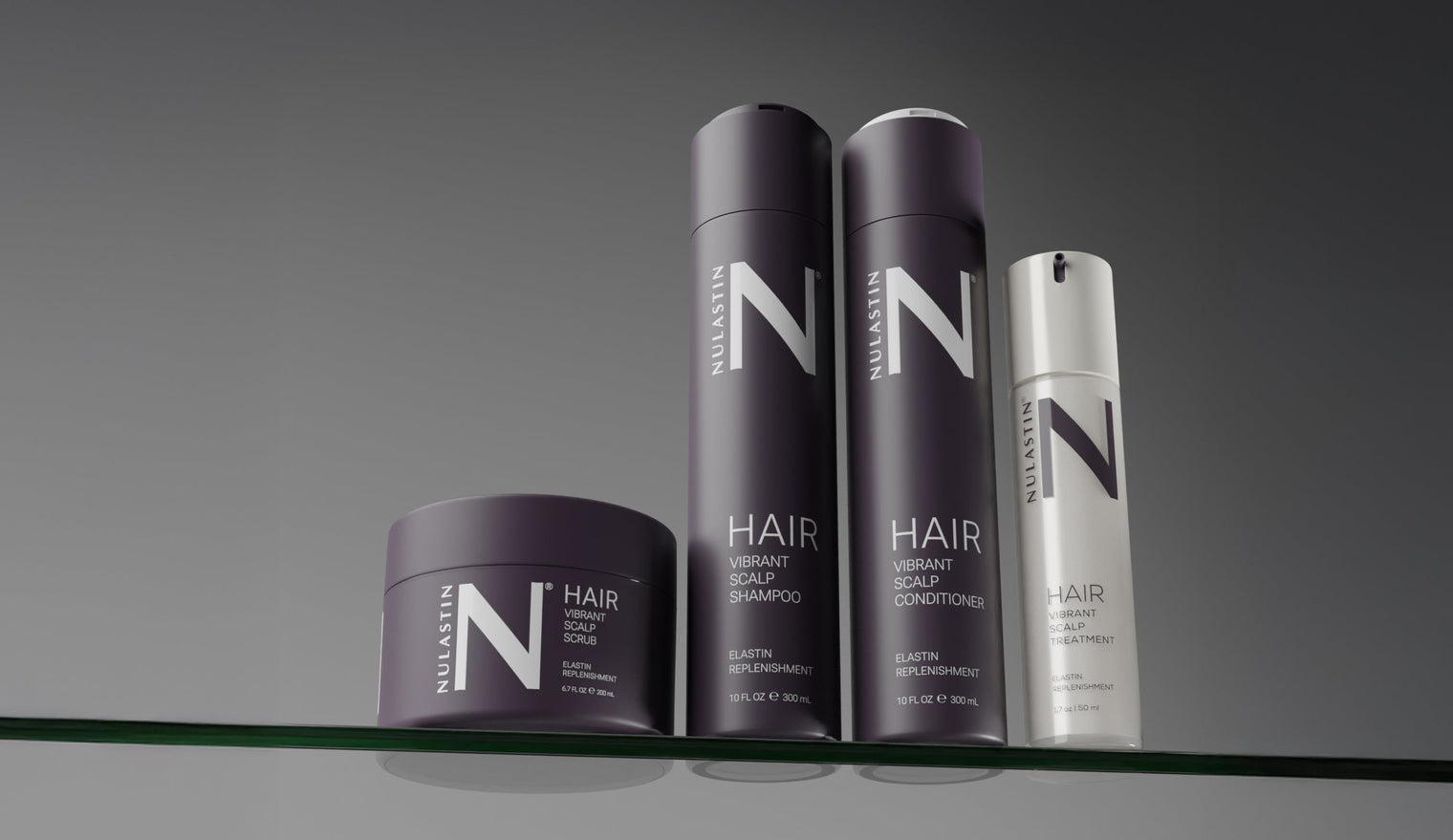 Front view of four NULASTIN Vibrant Scalp products, scrub, shampoo, conditioner, and treatment, with dark purple packaging and large N logo on a glass shelf