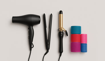 Top view of hair styling tools: black dryer, black flat iron, gold curling iron and colorful rollers on pale background