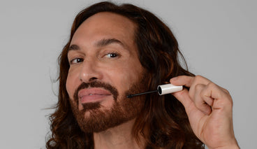 Man applying beard serum wand to trimmed beard against plain gray background