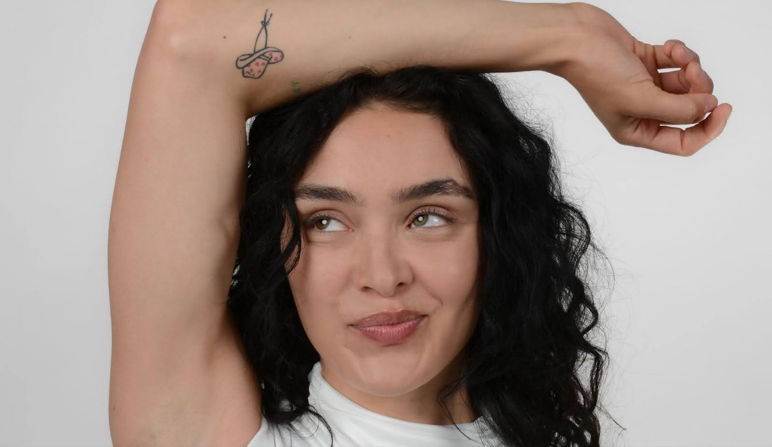 Young woman smiling with raised arm showing long curled eyelashes against a plain light background