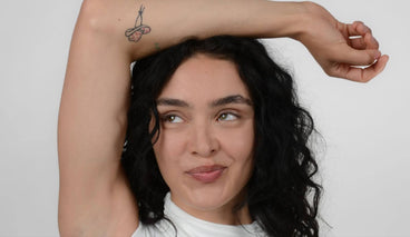 Young woman smiling with raised arm showing long curled eyelashes against a plain light background
