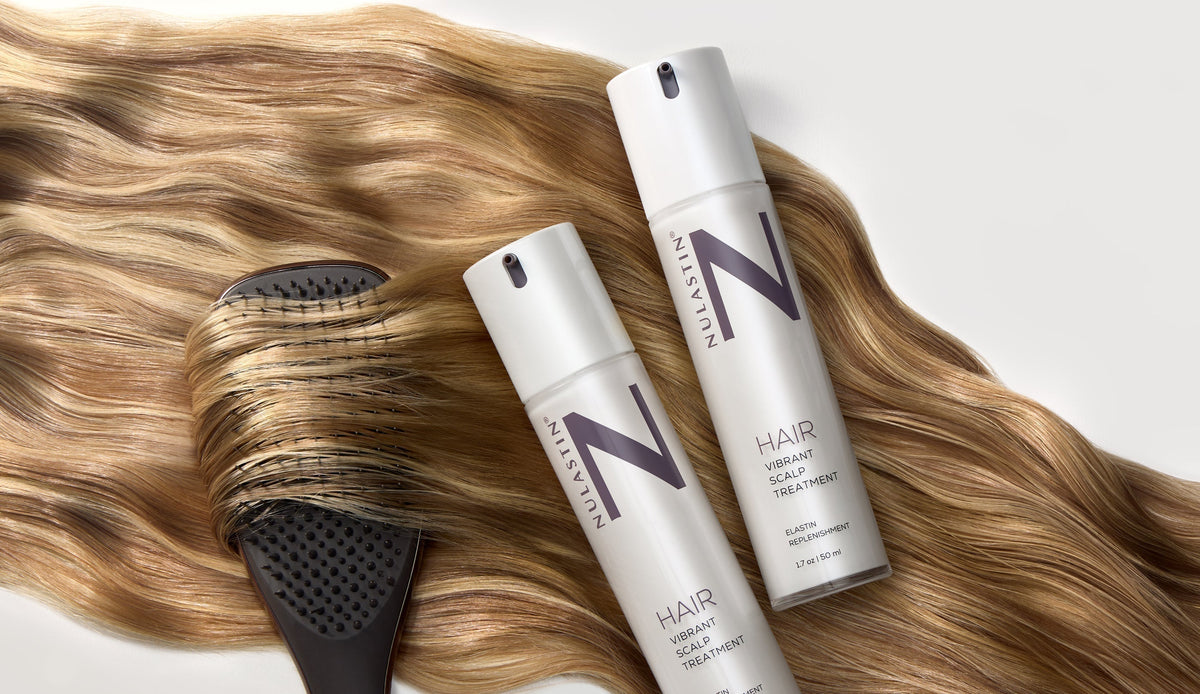 Close-up of NULASTIN Hair Vibrant Scalp Treatment bottles with pump dispensers, a hairbrush, and flowing hair
