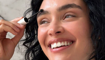 Woman applying brow serum with an applicator while smiling