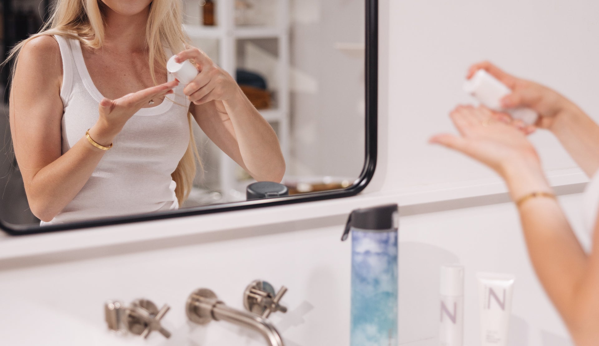 A blonde woman wearing gold jewelry applies NULASTIN® moisturizer as part of her daily skin regimen. 