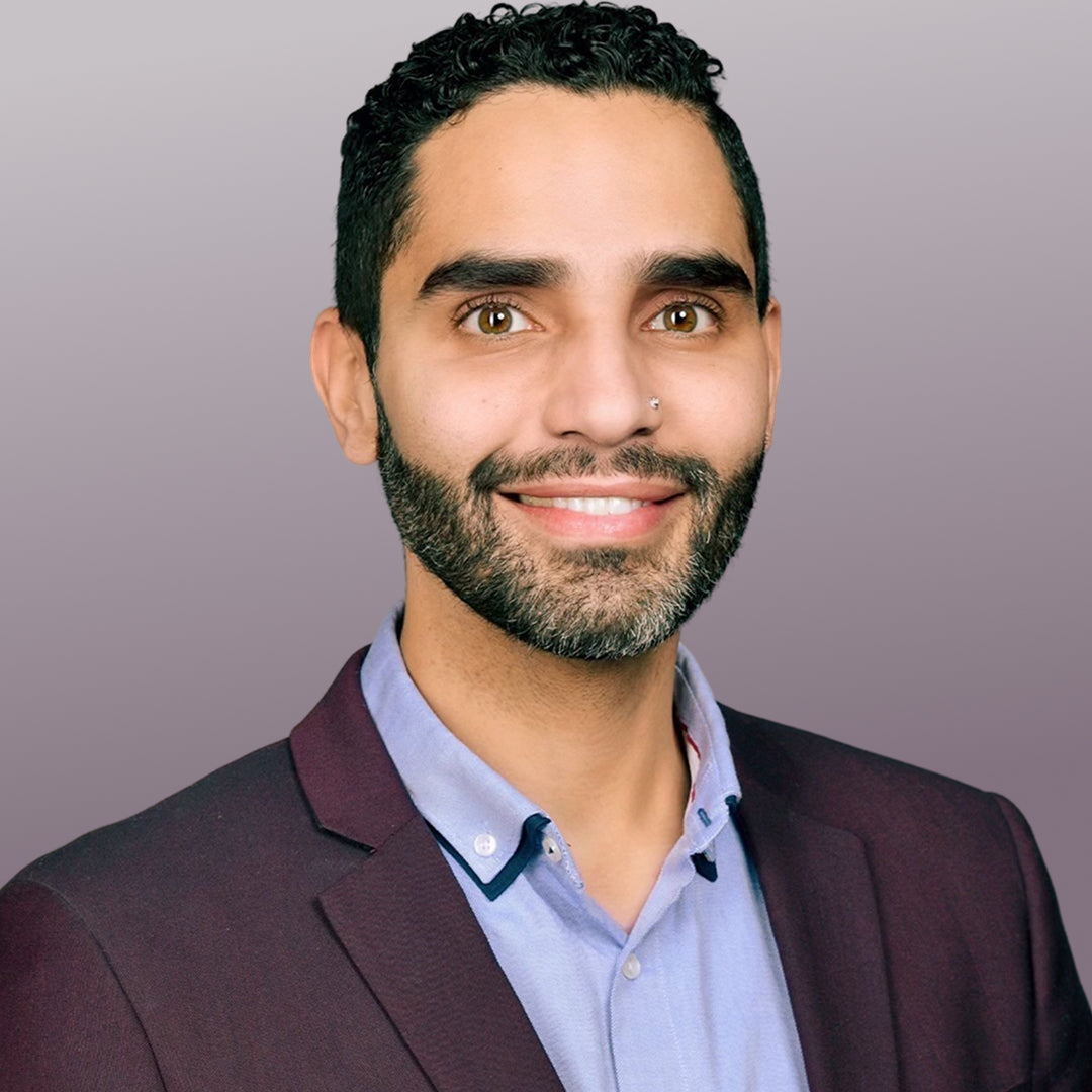 Dr. Omer Ibrahim smiling headshot, dermatologist in a maroon blazer and light blue shirt against a soft purple gradient background