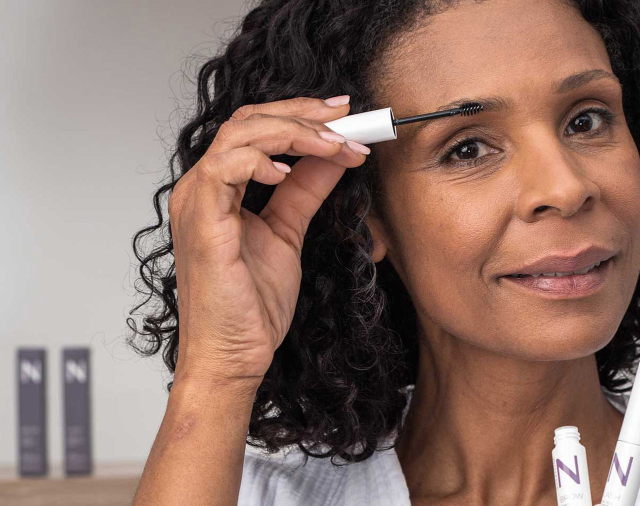 Woman with a shy smile applying Nulastin Brow Shape Altering serum