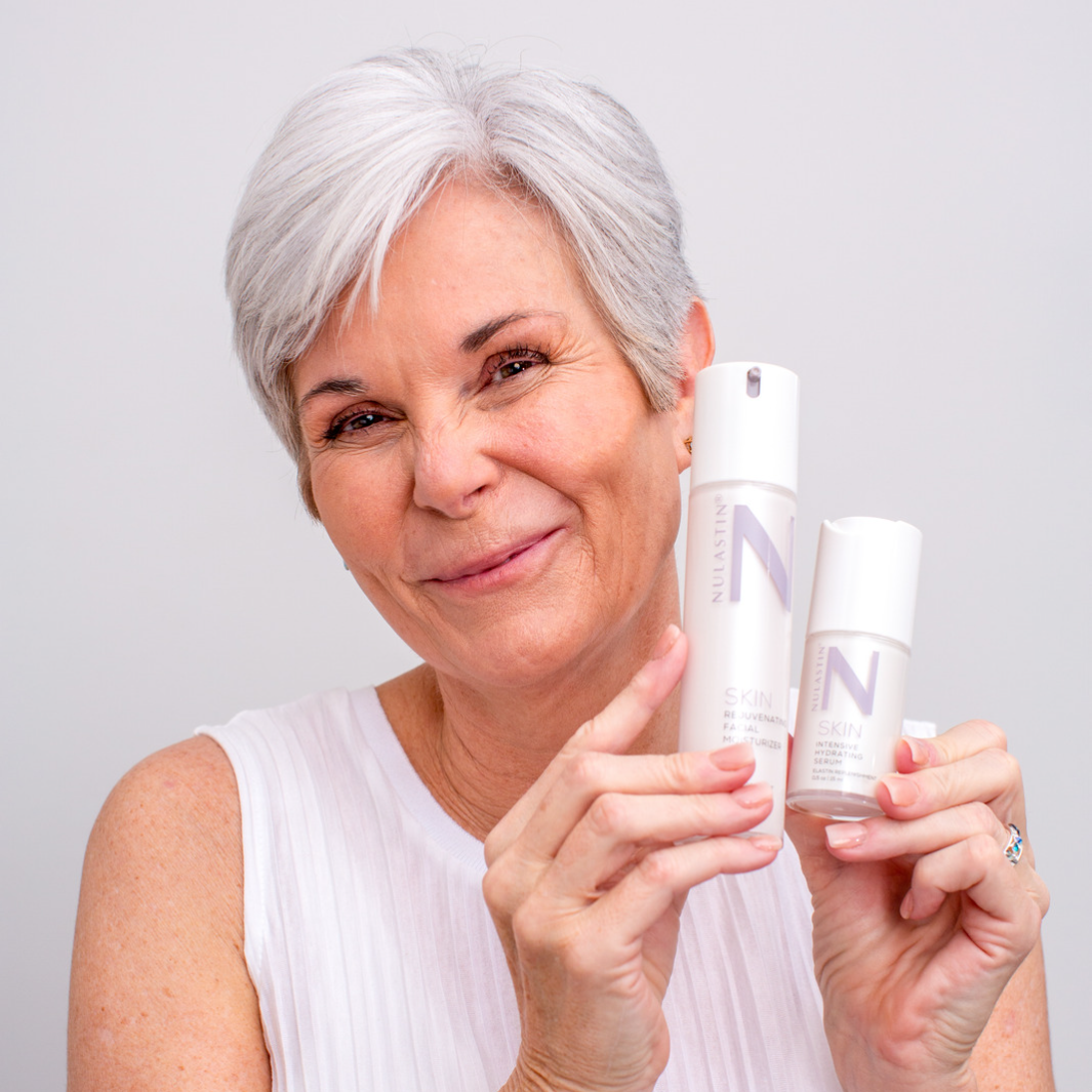 Woman with glowing skin holding two NULASTIN skincare bottles against white background