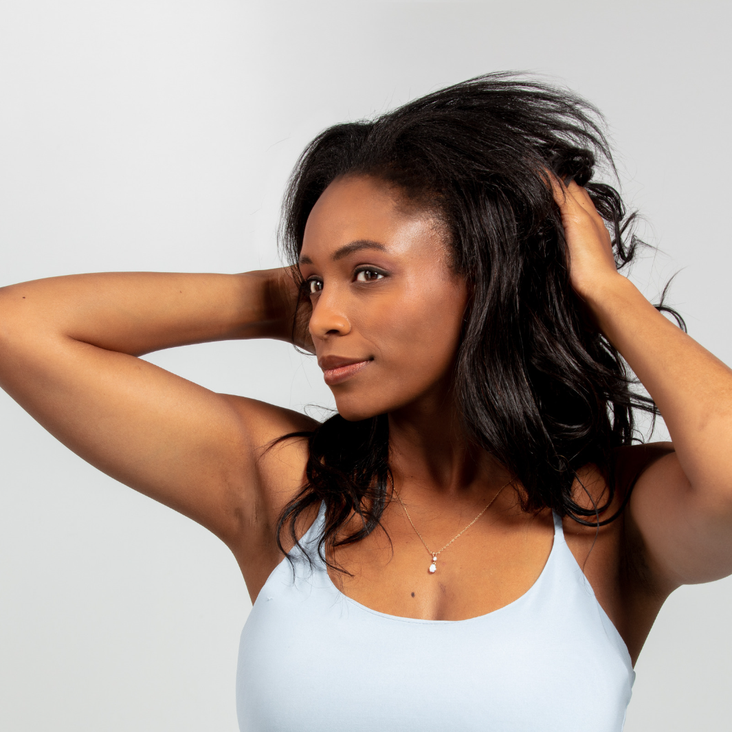 Woman with Dark Wavy hair putting hair product in hair against white background