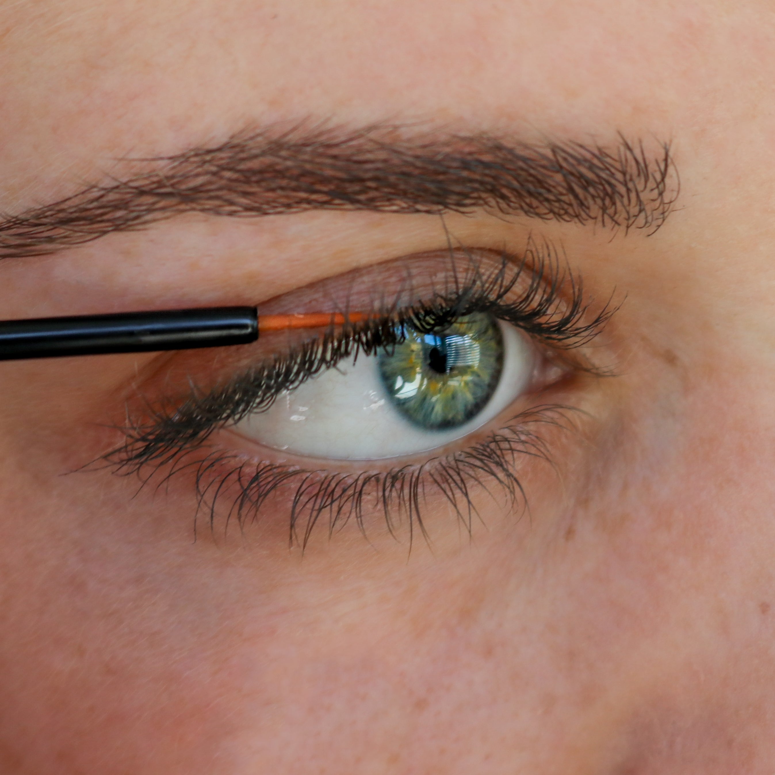 Woman with green eyes applying lash serum to skin