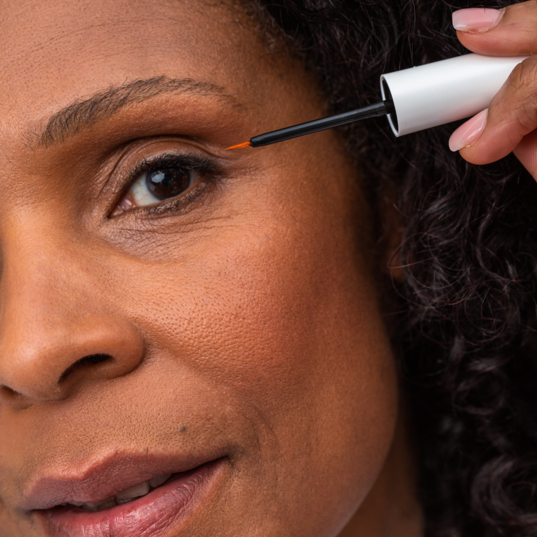 Close up of woman with dark hair applying lash serum to eyelashes 