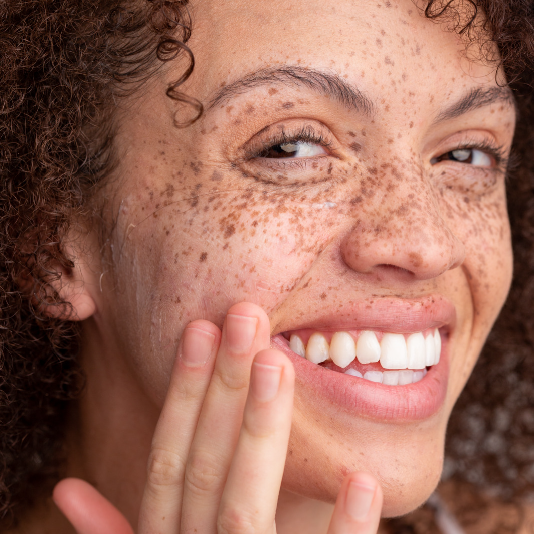 Woman with big smile applying NULASTIN skin cleanser to face