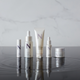 Five travel size product bottles on wet reflective surface against white background 