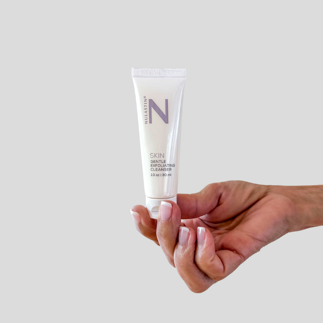 Hand holding NULASTIN travel size exfoliating cleanser white bottle