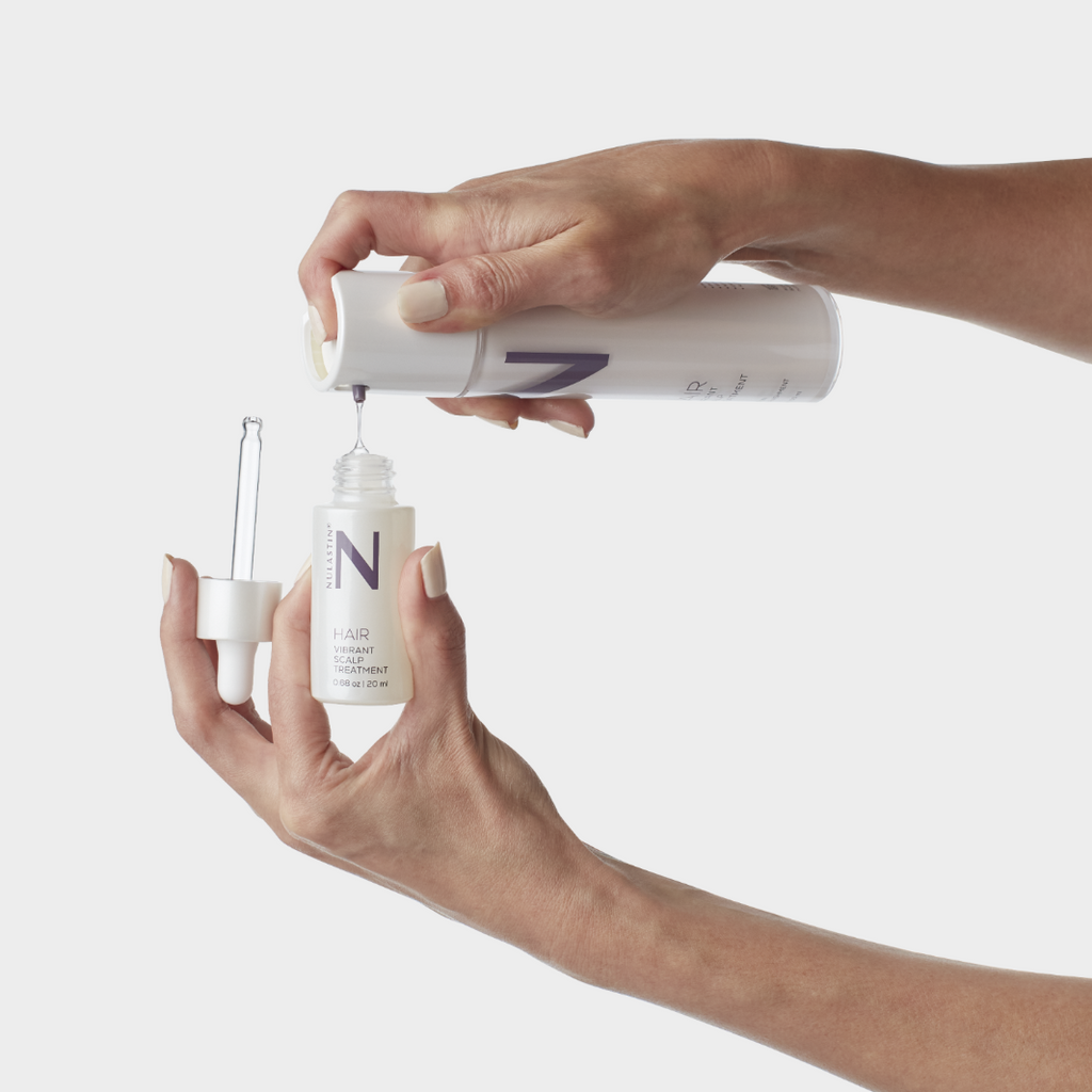 Hands filling small bottle with hair product from a larger bottle against white background 