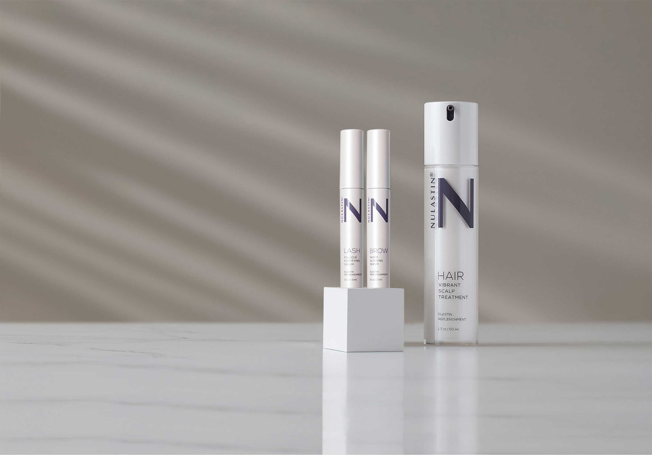 Nulastin Solution Serums trio featuring lash brow and hair on marble tile with classy sand colored backdrop