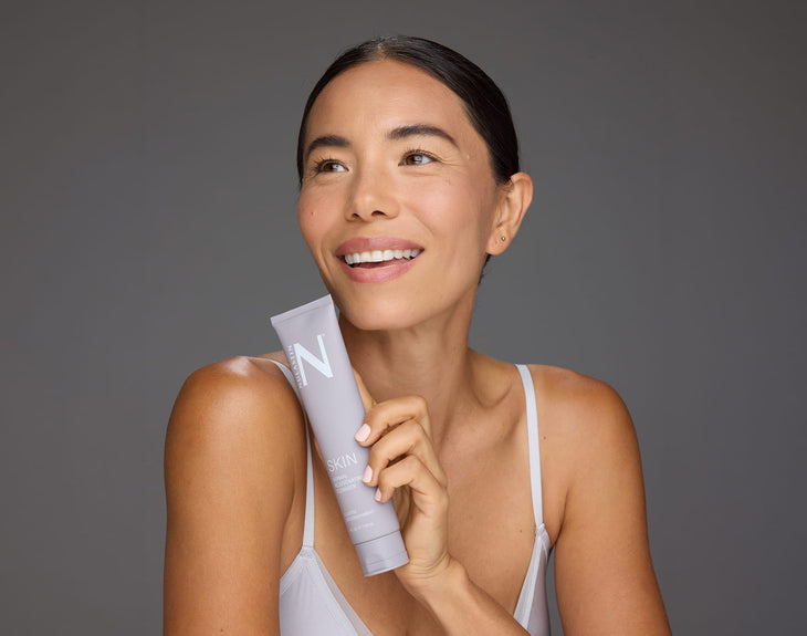 Three-quarter view of Dermal Rejuvenating Cleanser tube held by a model showing the N logo and front label against a neutral gray background