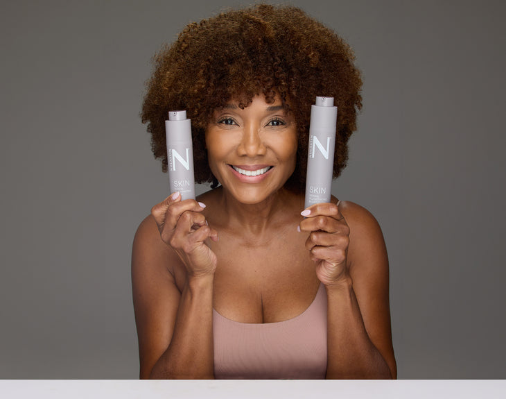 Front view of Dermal Rejuvenating Moisturizer bottles showing airless pump packaging held by a smiling woman against a gray background