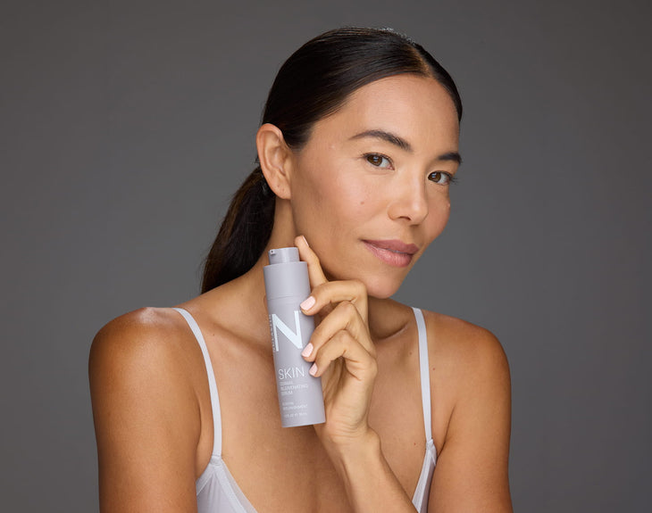 Front view of Dermal Rejuvenating Serum bottle showcasing airless pump packaging held by model against a neutral gray background