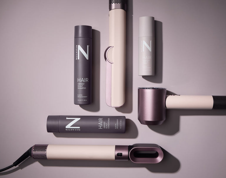 Flat lay of NULASTIN hot tools and hair care bottles showing three styling tools and two product bottles on mauve background